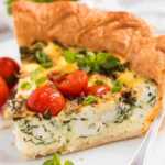 Slice of tomato spinach feta quiche on plate.