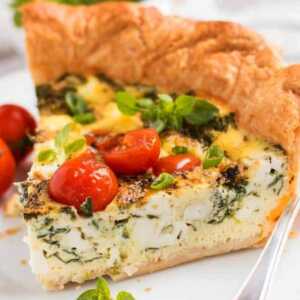 Slice of tomato spinach feta quiche on plate.