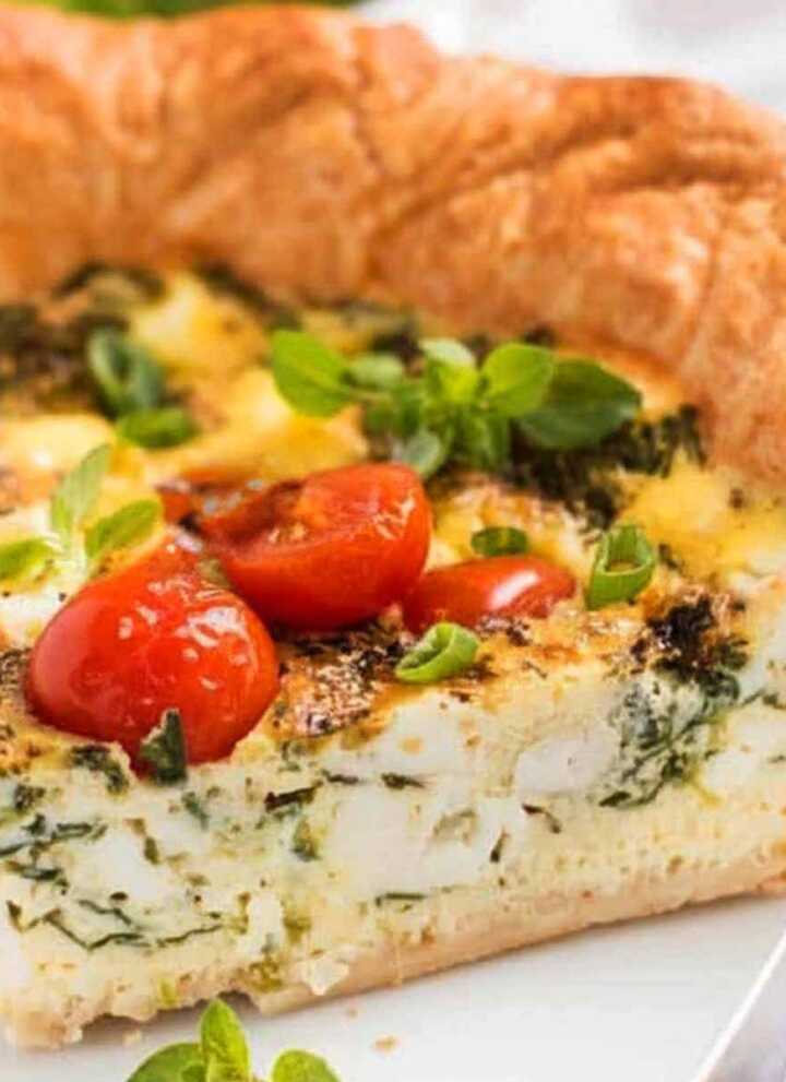 Slice of tomato spinach feta quiche on plate.