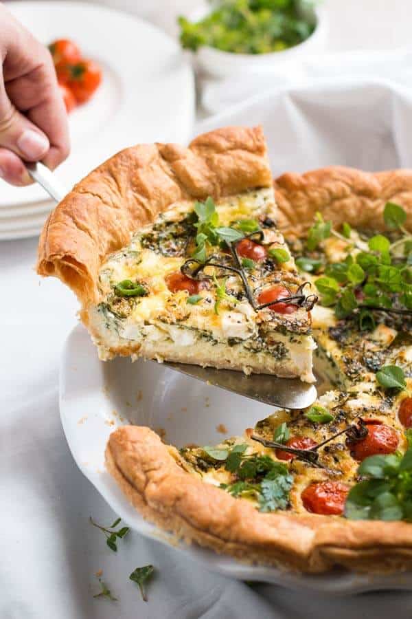 female hand holding cake scoop with a slice of feta quiche