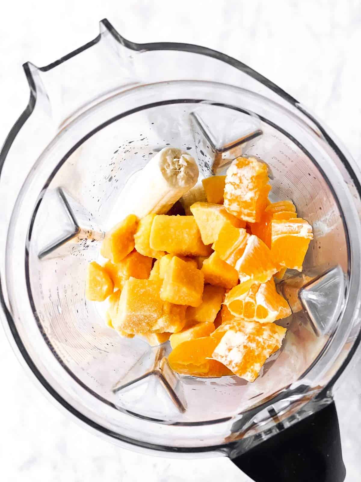 overhead view of mixer cup with ingredients for a mango smoothie