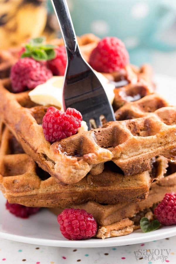 stack of healthy banana oatmeal waffles, garnished with banana slices and raspberries and with a fork stuck in