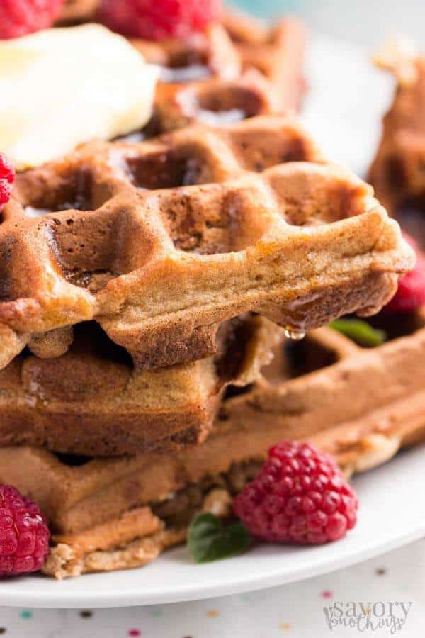 close up photo of a stack of oatmeal waffles with bananas and raspberries around