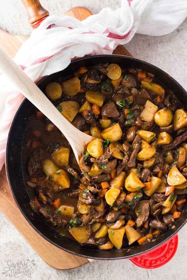 Potato, beef tips and gravy skillet on a wooden board with a wooden spoon and a tea towel