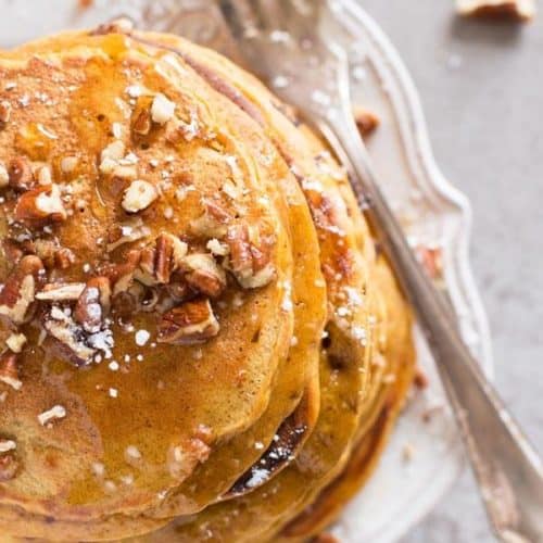 top down view on pumpkin pancakes and fork on white plate with chopped pecan nuts