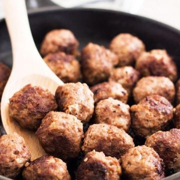 close up photo of pan-fried meatballs in black cast iron skillet with wooden spoon