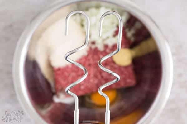 close up of hand mixer over bowl of meatball ingredients