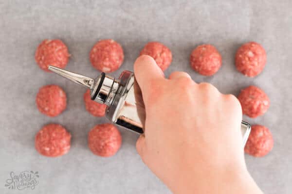 female hand drizzling oil over uncooked meatballs