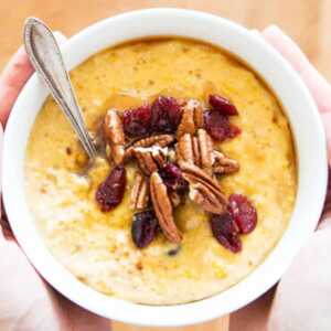 white bowl filled with pumpkin oatmeal topped with pecans and cranberries