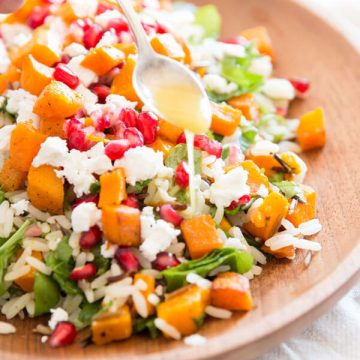 female hand holding a spoon to drizzle dressing over a wild rice salad