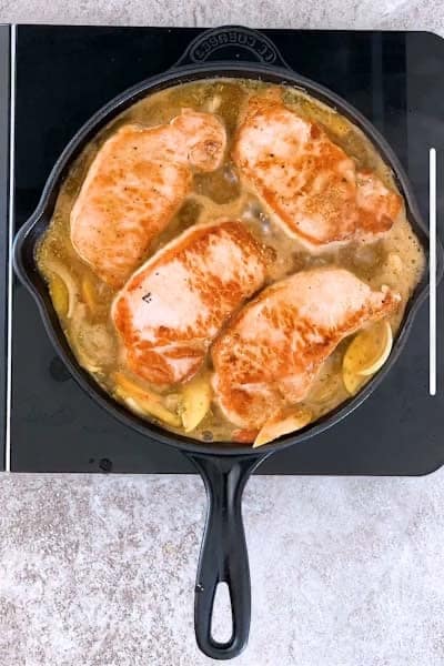 Cast iron skillet filled with apples, onions, gravy and pork chops