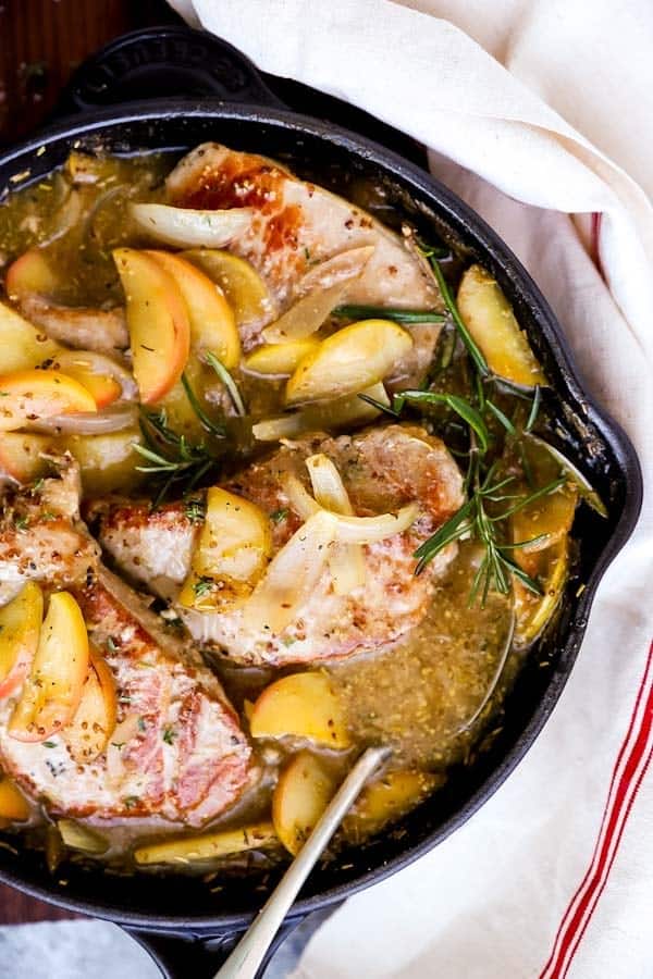 Close up of a skillet filled with pork chops, apples and onions