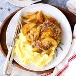 plate with apple pork chops and mashed potatoes, next to a second plate and a tea towel