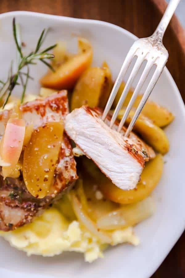 sliced open pork chops on a plate with gravy, apples, onions and mashed potatoes