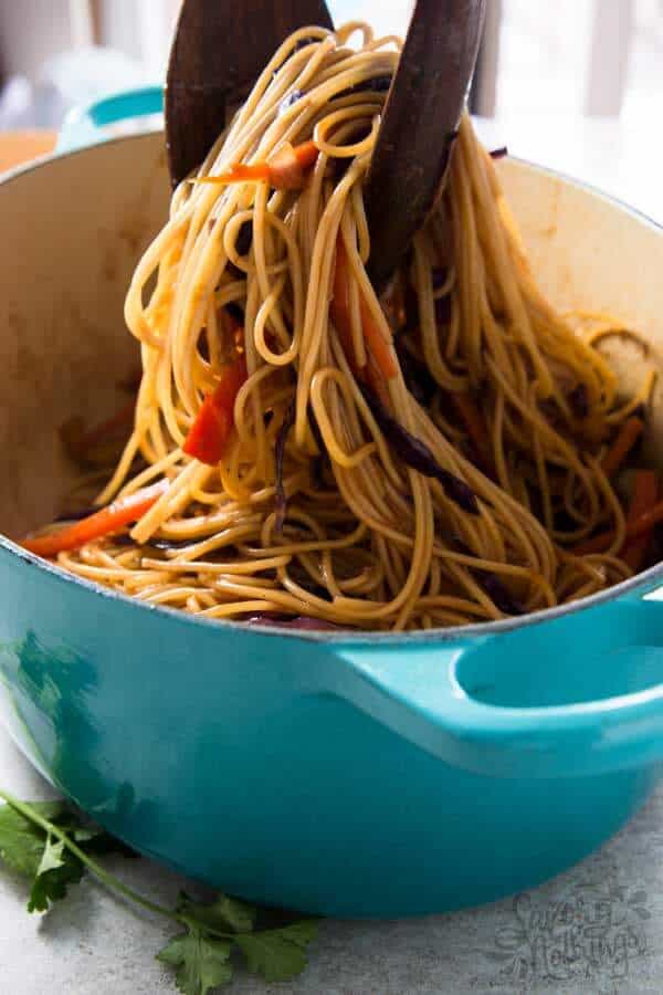 wooden tongs pulling chicken noodles out of blue dutch oven