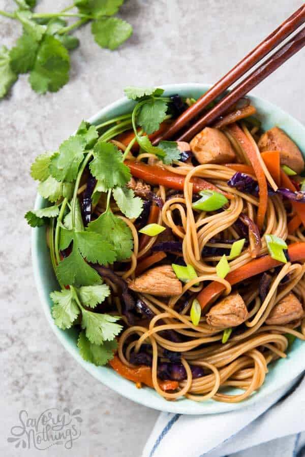 top down view on chicken noodles topped with fresh cilantro in light blue bowl with wooden chopsticks