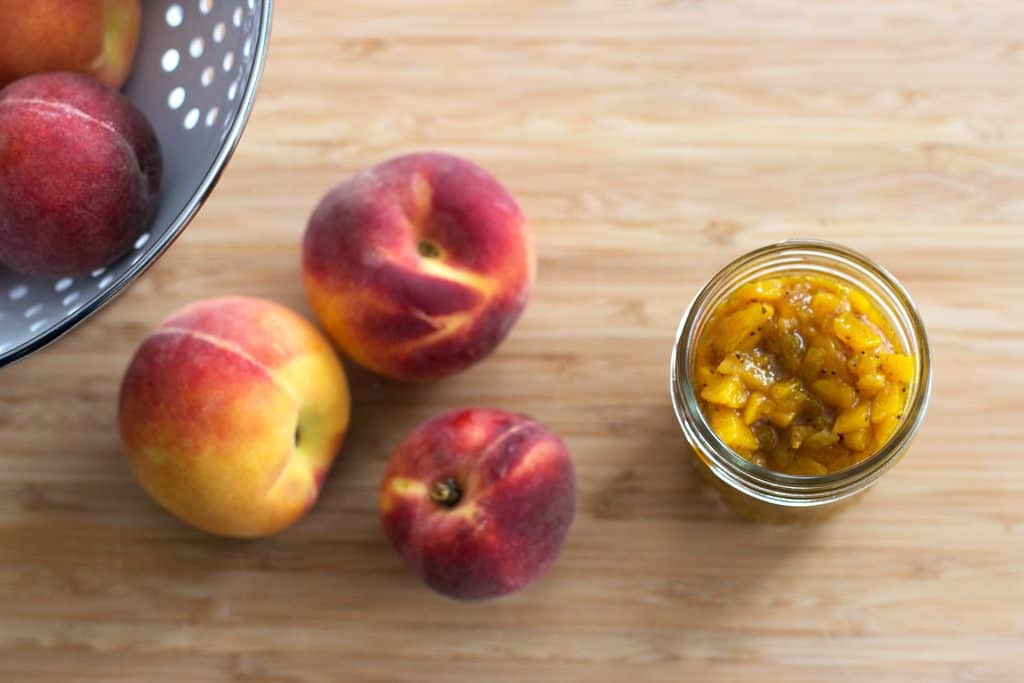 top down view on fresh peaches and a jar of peach chutney