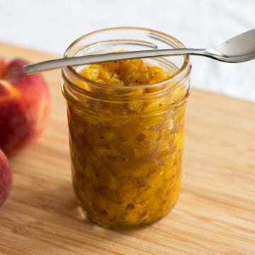 jam jar filled with chutney next to fresh peaches