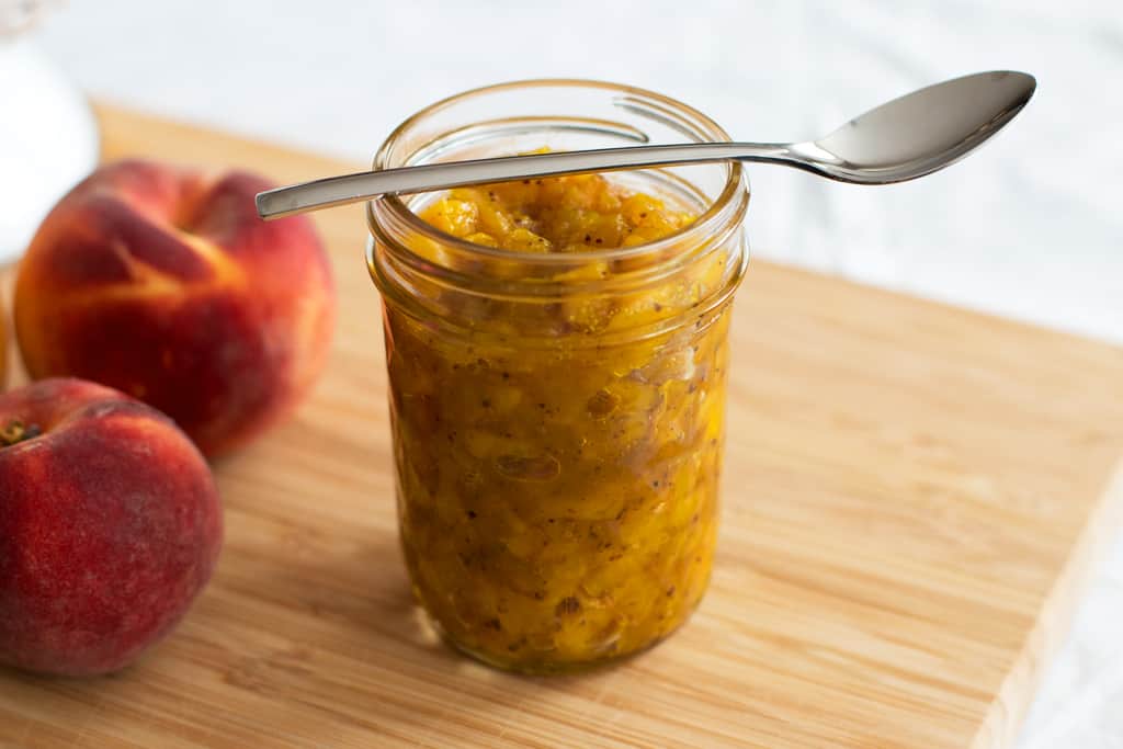 jam jar filled with chutney next to fresh peaches