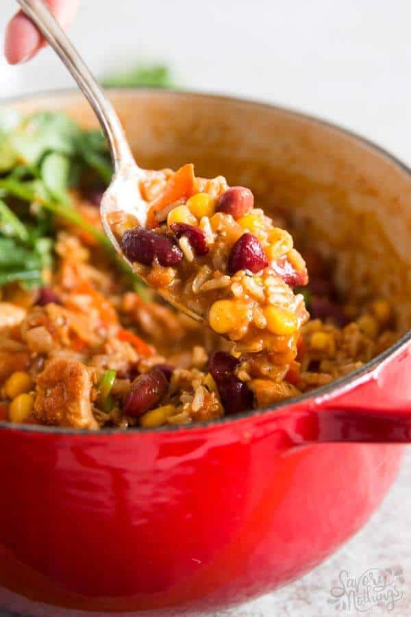 chicken and rice on spoon in front of a red Dutch oven