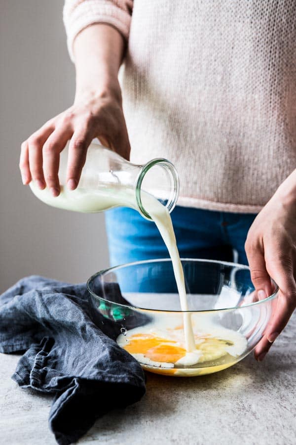 woman pouring milk into bowl with eggs