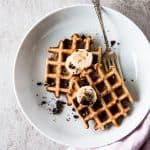 top down view on two banana waffles on white plate with a fork