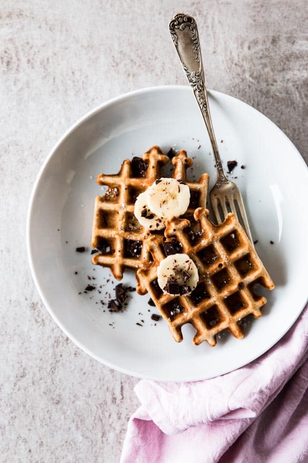 top down view on two banana waffles on white plate with a fork