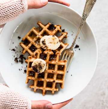 overhead view on female hands holding white plate with banana waffles