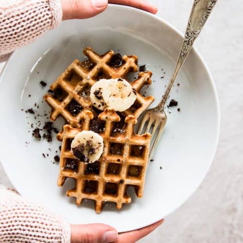 overhead view on female hands holding white plate with banana waffles