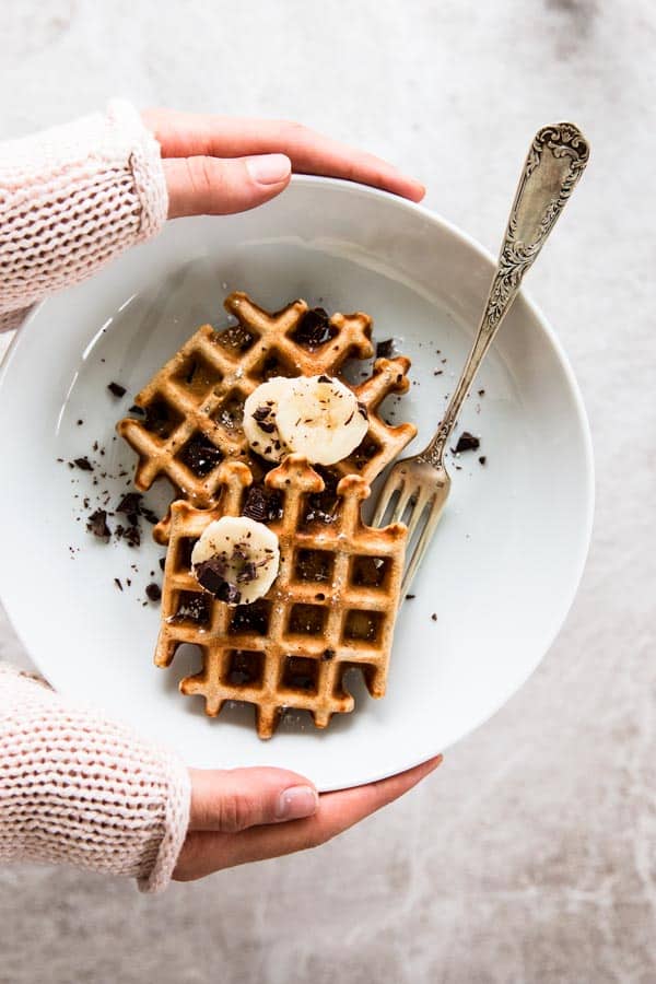 overhead view on female hands holding white plate with banana waffles