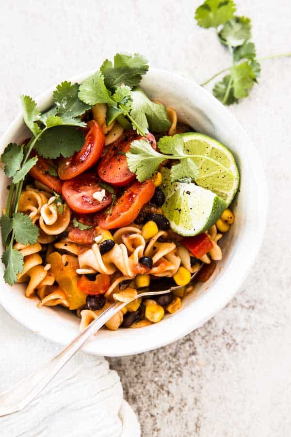 white bowl filled with enchilada pasta and garnished with fresh cilantro and lime