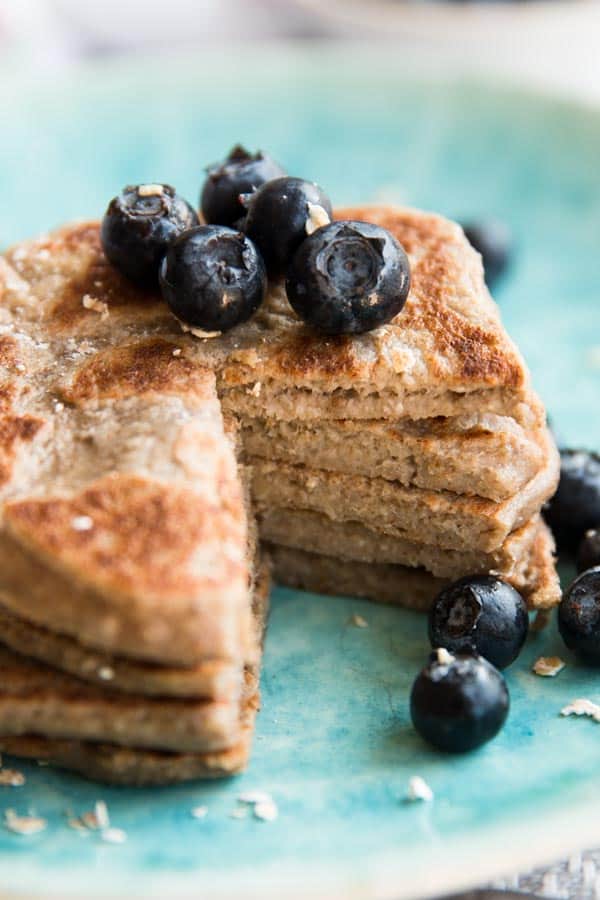 cut open stack of vegan banana pancakes on blue plate with fresh blueberries