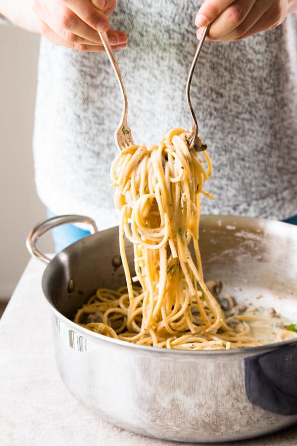 woman in grey shirt lifting mushroom pasta out of pan