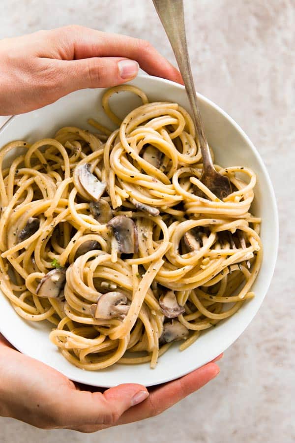 female hands holding mushroom pasta in white bowl with fork