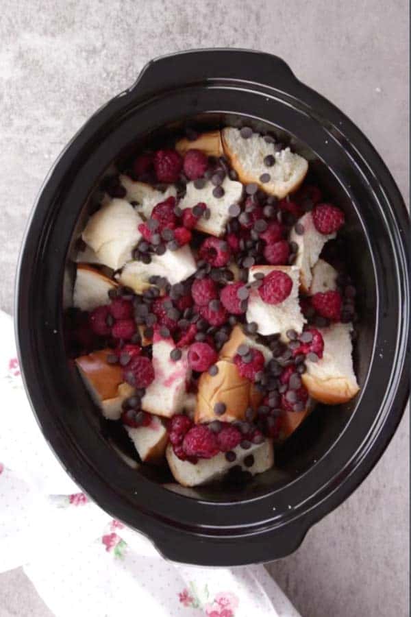 black crock from a slow cooker filled with cubed challah bread, raspberries and chocolate chips