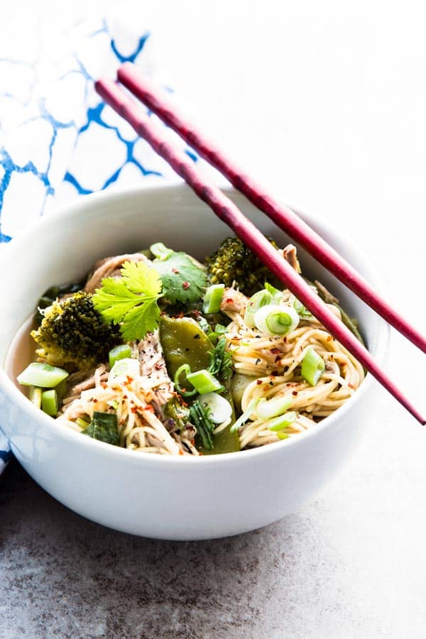 asian pork and noodles in white bowl with red chopsticks