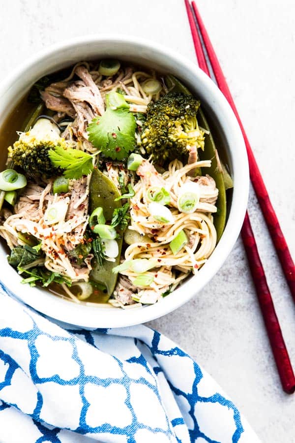 top down view on asian pork noodles in white bowl next to red chopsticks