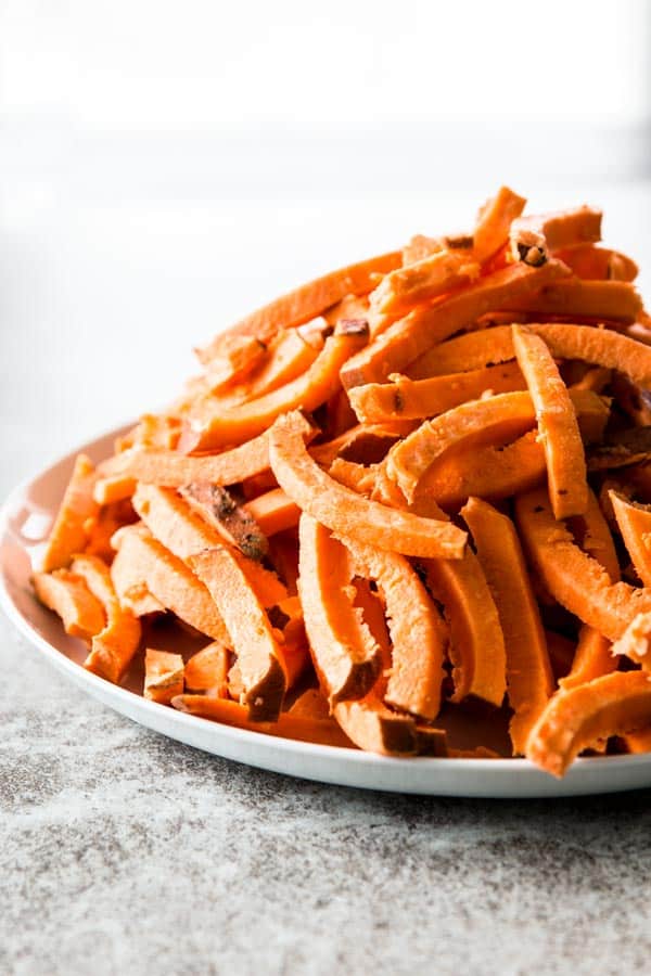 file of raw sweet potatoes cut into fries on white plate