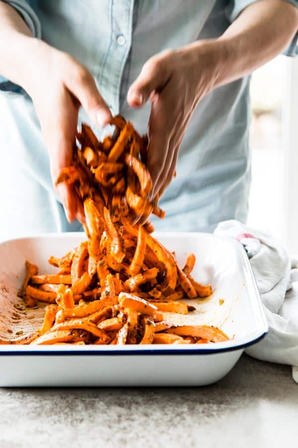 woman in blue shirt tossing sweet potato fries in white enamel bowl