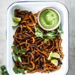 top down view on white enamel dish filled with baked sweet potato fries and a small white bowl with avocado dipping sauce