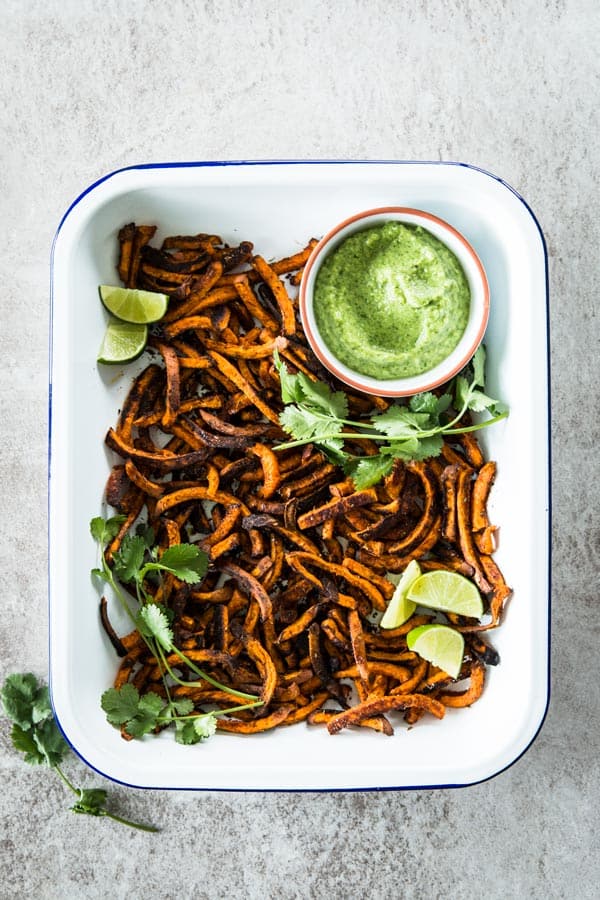 top down view on white enamel dish filled with baked sweet potato fries and a small white bowl with avocado dipping sauce