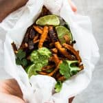 overhead view on female hands holding sweet potato fries wrapped in baking parchment