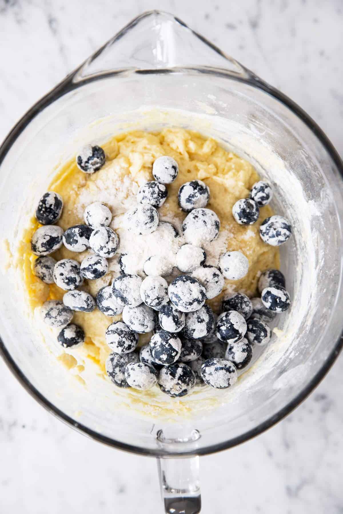 glass bowl with plain muffin batter and floured blueberries on top