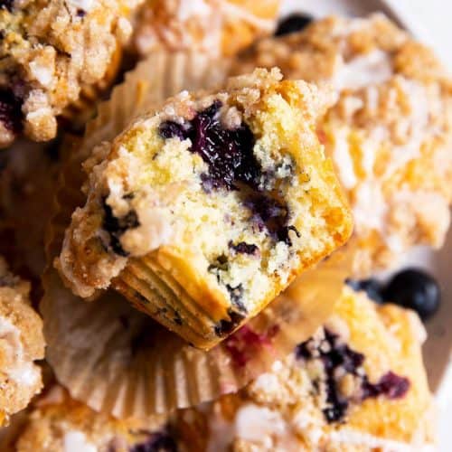 overhead view of blueberry muffin with bite taken out on plate with more muffins