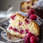 slice of raspberry cake on floral plate with fresh raspberries and silver fork