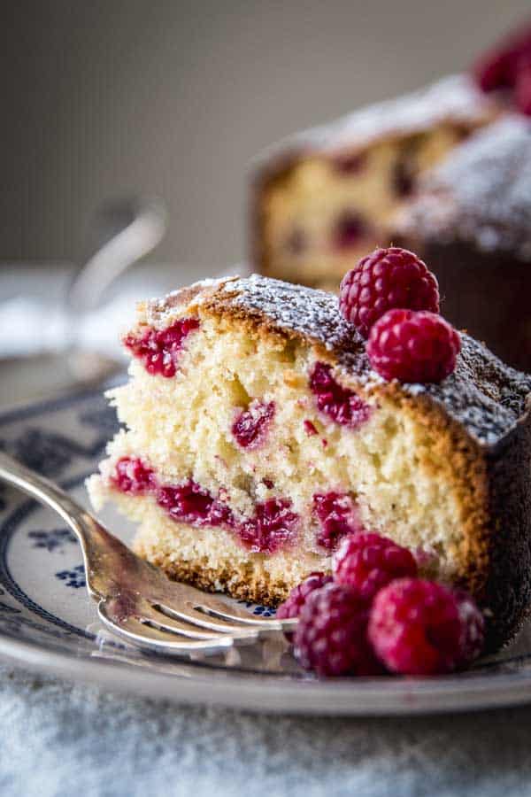 slice of raspberry cake on floral plate with fresh raspberries and silver fork