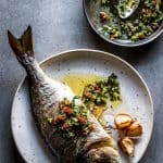 overhead view on baked whole baked fish on white plate with caper salsa