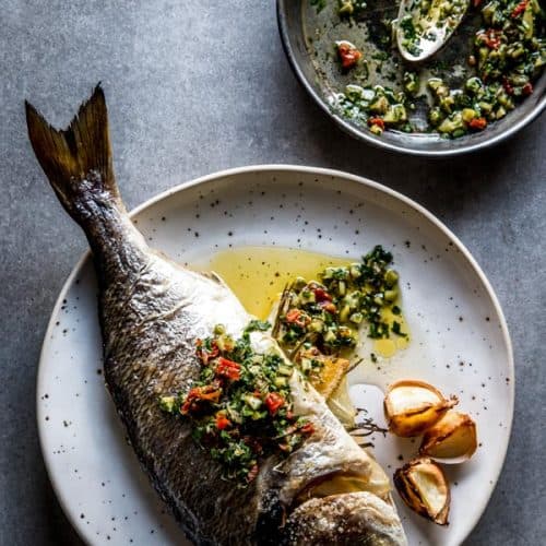 overhead view on baked whole baked fish on white plate with caper salsa
