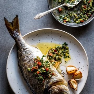 overhead view on baked whole baked fish on white plate with caper salsa