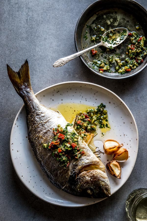 overhead view on baked whole baked fish on white plate with caper salsa